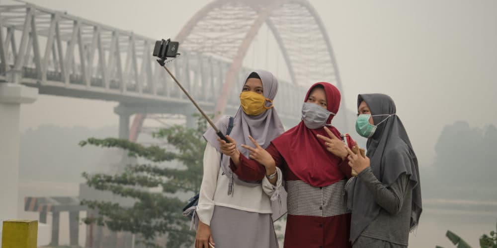 Waldbrände: Frauen posieren mit Masken vor verrauchter Brücke