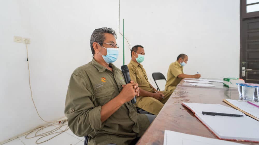 drei Männer mit Maske während einer Farmer Field School im Seminarraum