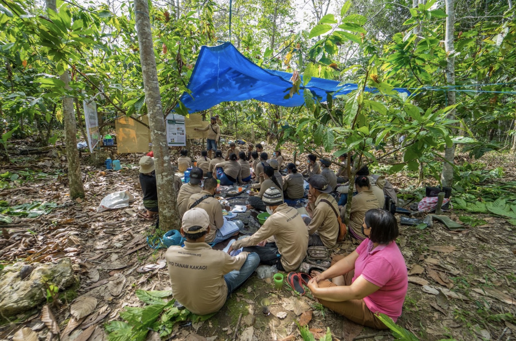 Teilnehmende der Cacao Field School sitzen im Wald auf dem Boden unter einer Plane