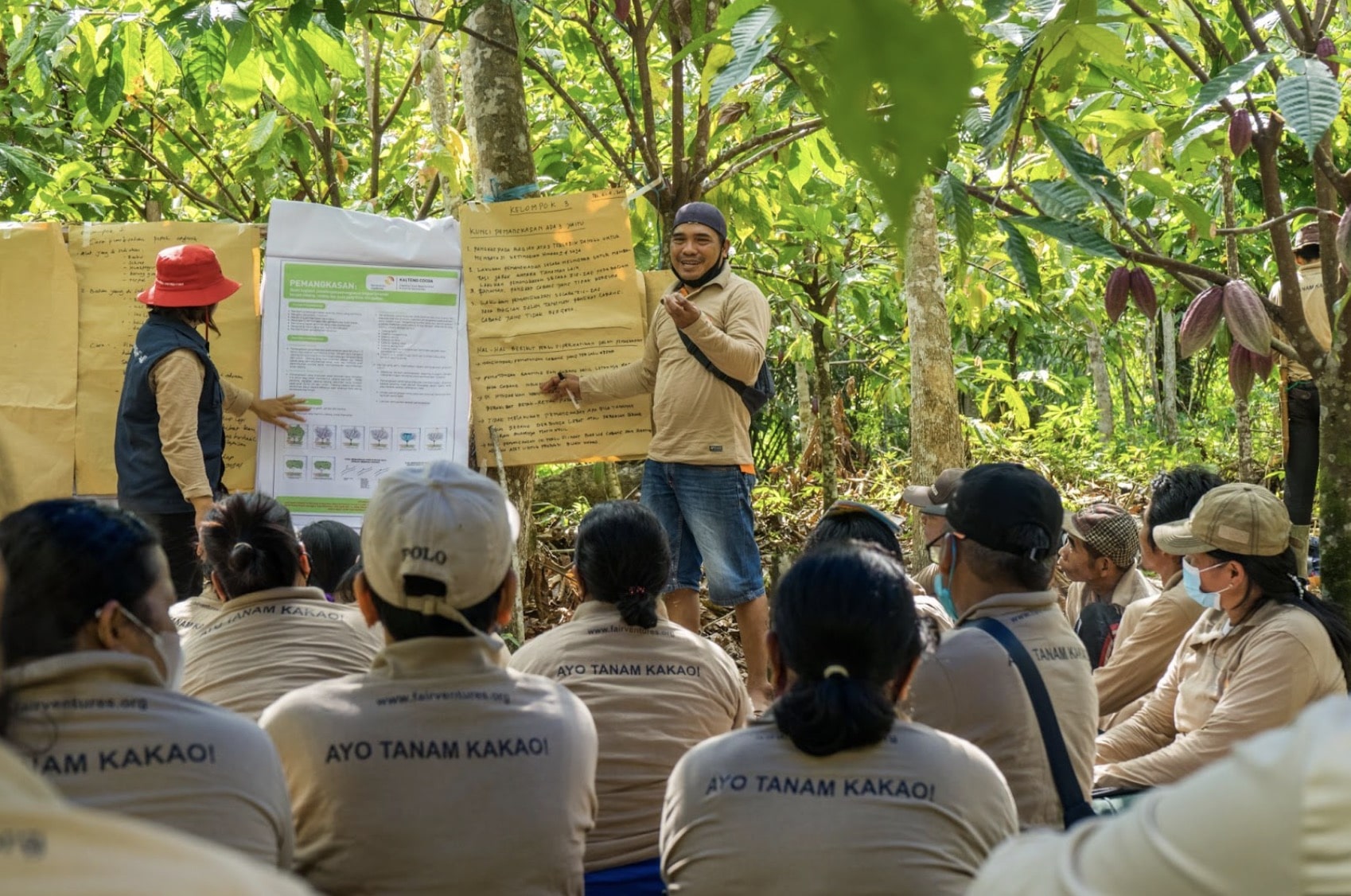 Trainer stands in front of group and points to his presentation in the forest