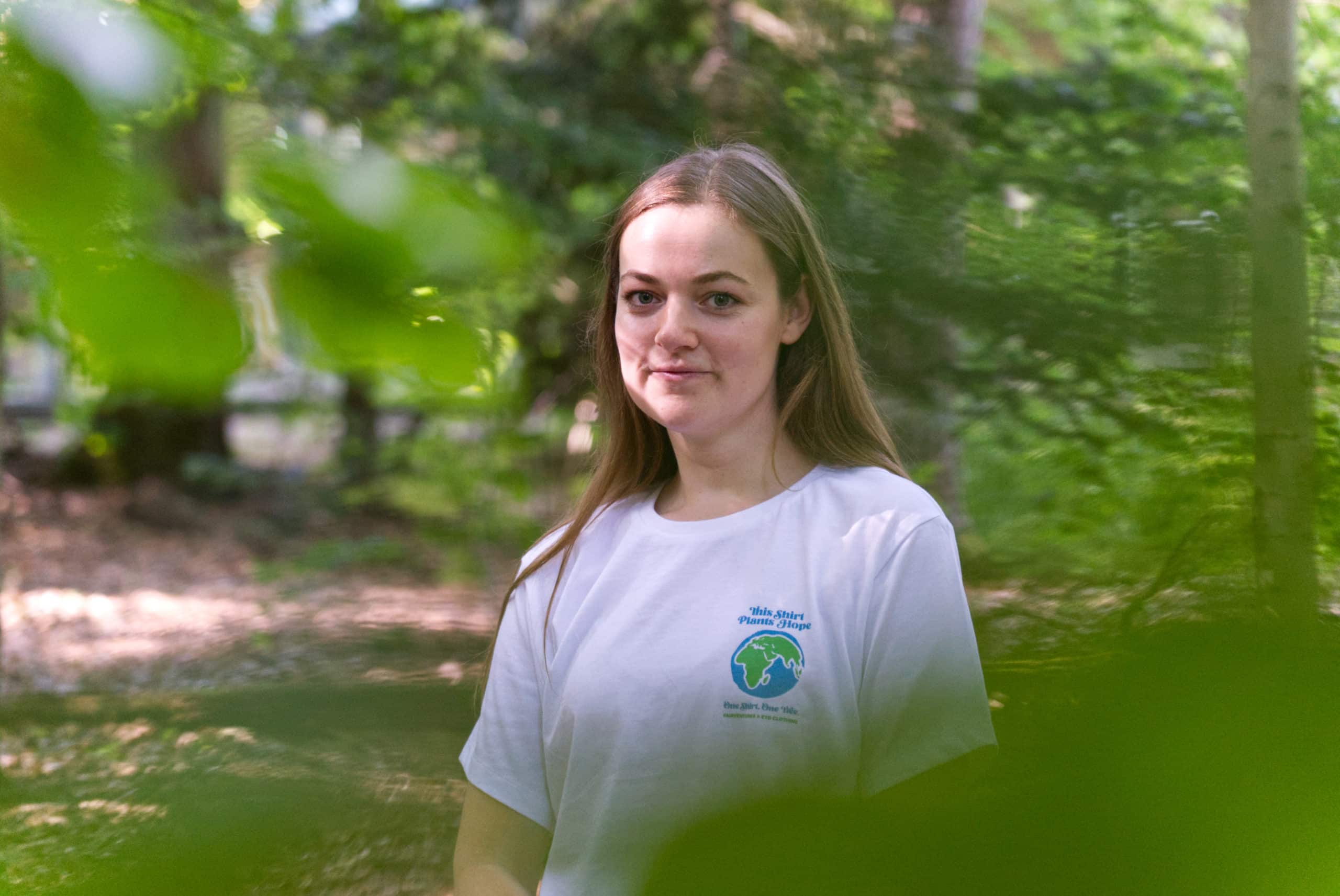 Hanna steht im Wald und trägt das #PlantHope22-Kampagnenshirt
